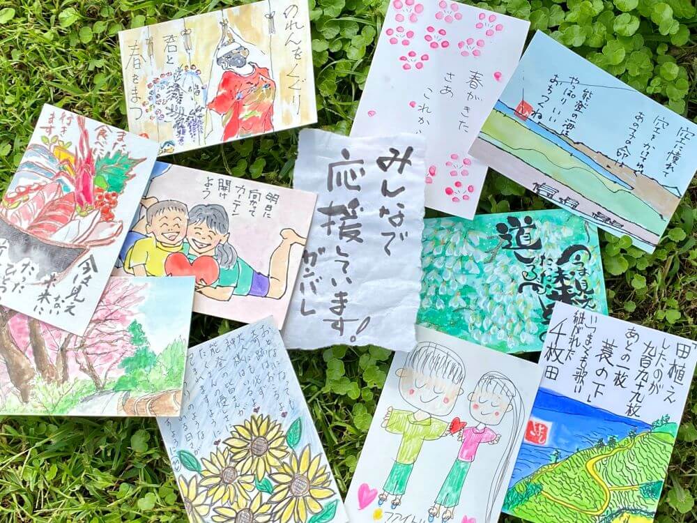 Assorted colorful handmade cards with drawings and handwritten notes spread on green grass.